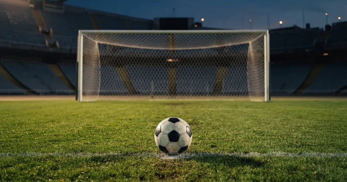 Ein Fußball liegt im Strafraum direkt vor dem Tor mit Netz, im Hintergrund leere Ränge bei Dämmerung.